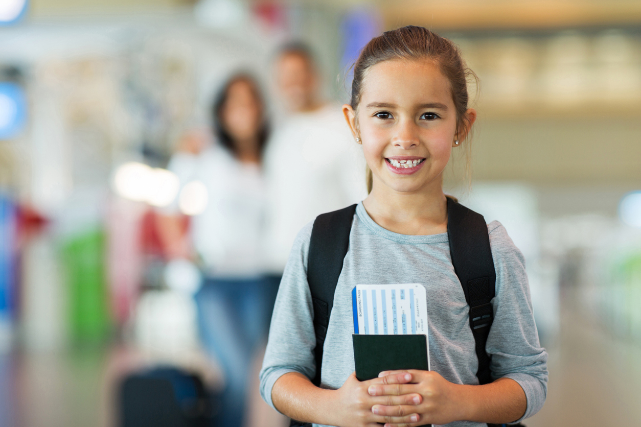 Linda menina, segurando o passaporte e cartão de embarque no aeroporto com os pais. Confira se criança pode acumular milhas.