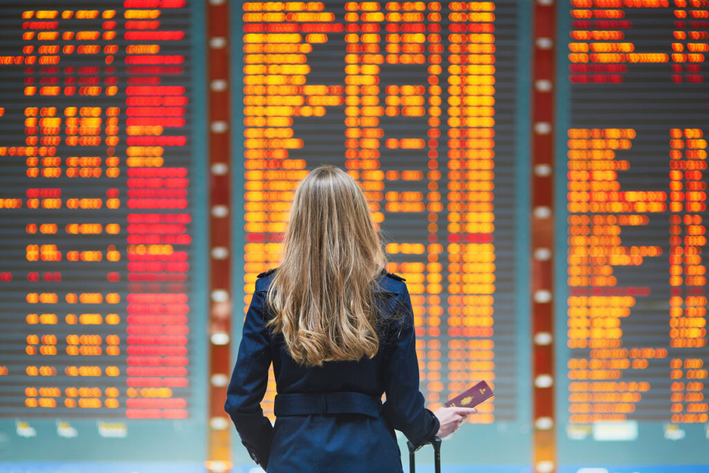 Jovem mulher olhando o painel de voos no aeroporto sobre as mudanças das regras smiles em relacao ao acumulo de milhas nos voos da GOL.