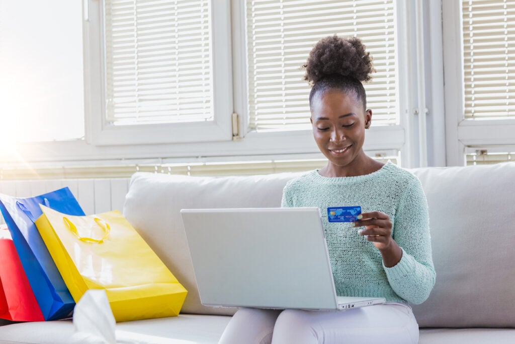 Mulher sentada na sala de estar, segurando um cartão de crédito fazendo compras online em seu notebook e aprendendo como ganhar dinheiro.