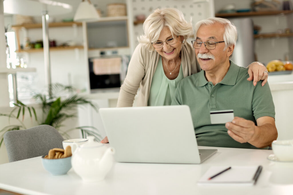 Casal de idosos feliz segurando o cartão de crédito fazendo compras online em seu notebook.