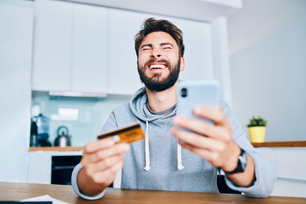 Homem de olhos fechados segurando celular e cartão de crédito, conferindo sobre seus pontos Mastercard.