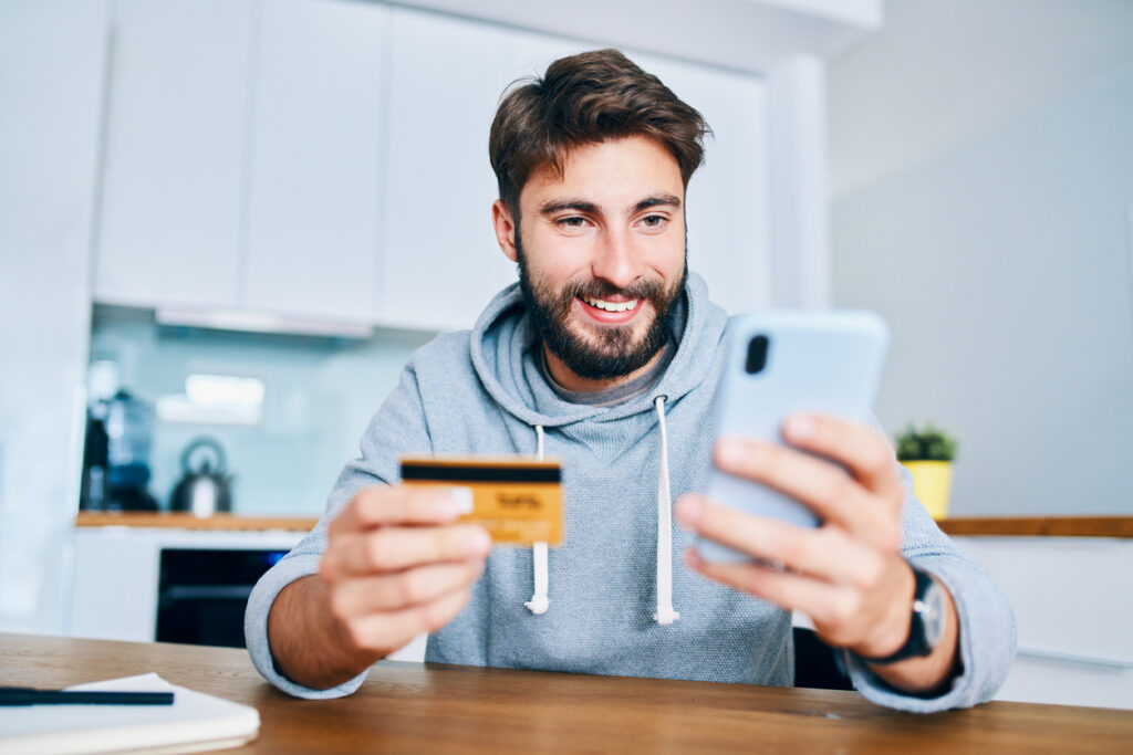 Homem segurando celular e cartão de crédito para acumular no programa de pontos Mastercard.