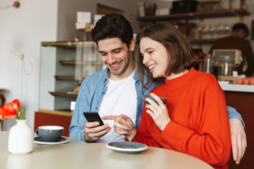 Jovem casal feliz utilizando o celular conferindo as dicas de como usar o App da Hot Milhas.